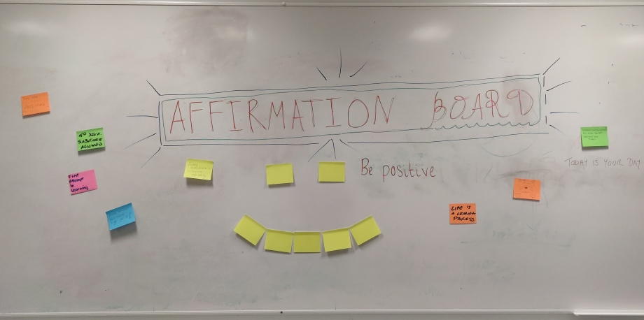 The image shows a whiteboard with yellow post-its arranged in a smile with coloured post-it notes around it