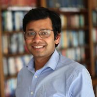 A profile image of a man with brown skin, dark hair and glasses in a light blue shirt