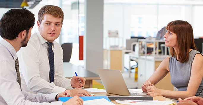 Woman talking to two male students at a desk