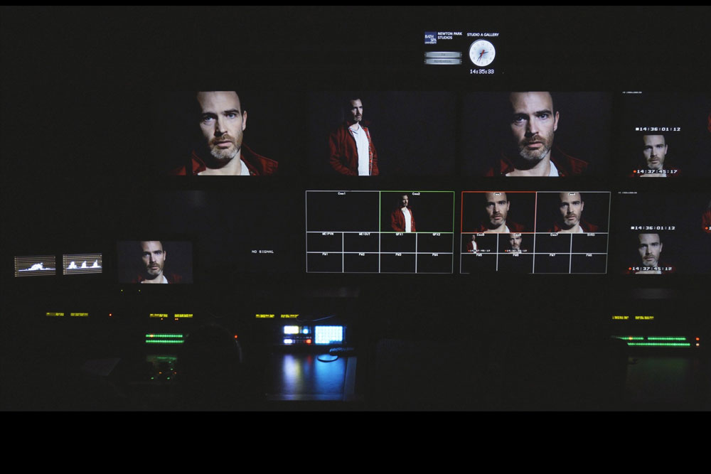 Multiple screens showing a mans face against a dark background