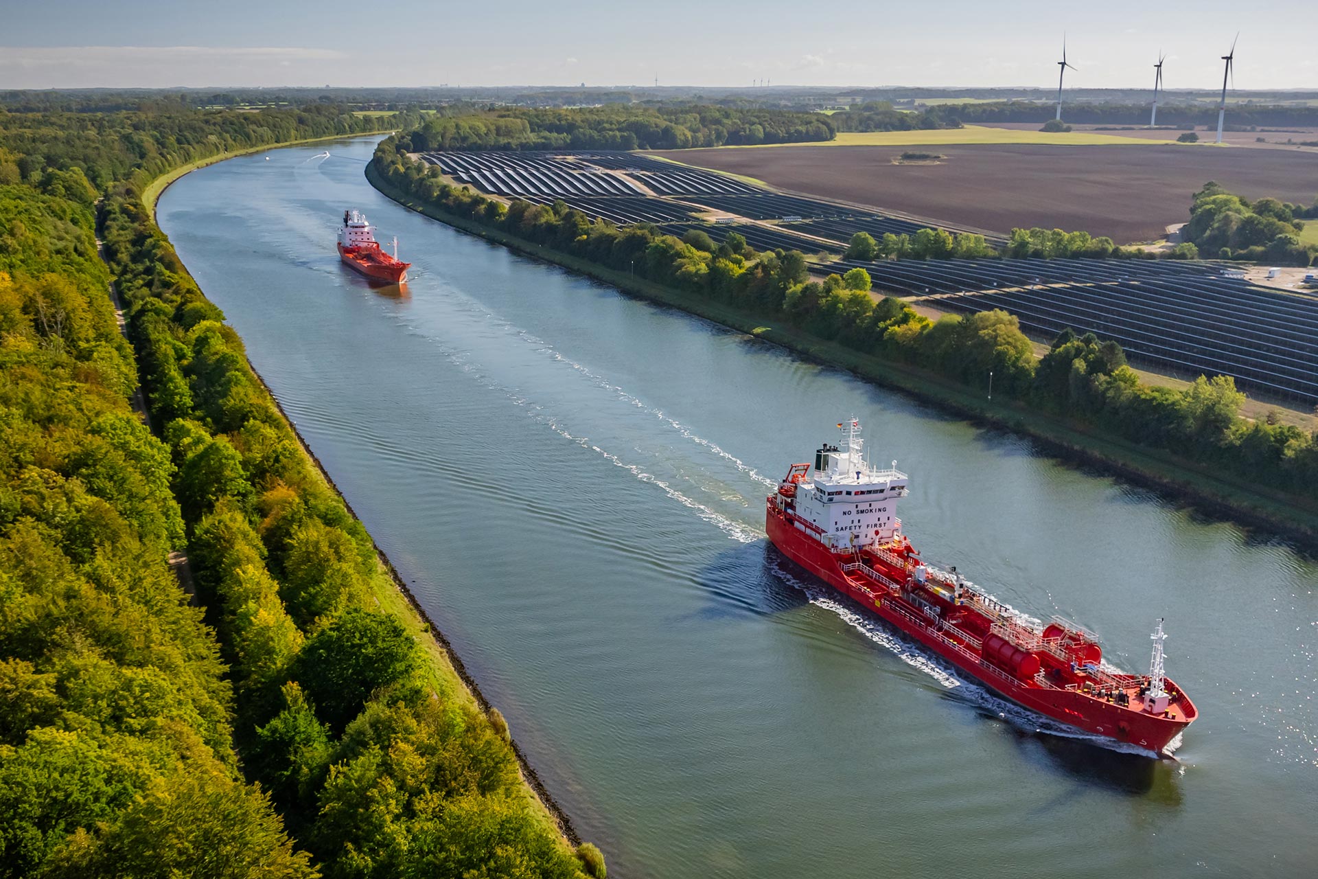 Tanker transporting fossil fuels along waterway, sailing past canal bordered by solar farm.