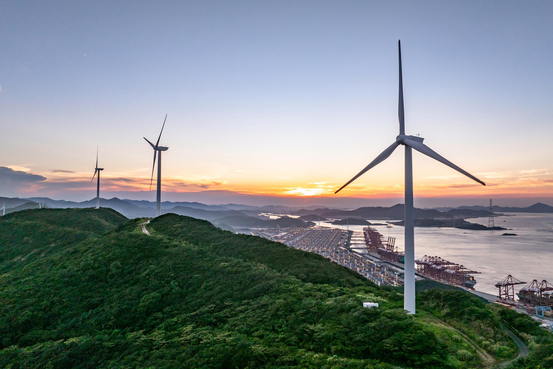 Wind turbines on a a coastal area with the sun setting in the background