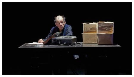 A man sitting at a desk with a tape recorder and cardboard boxes on it