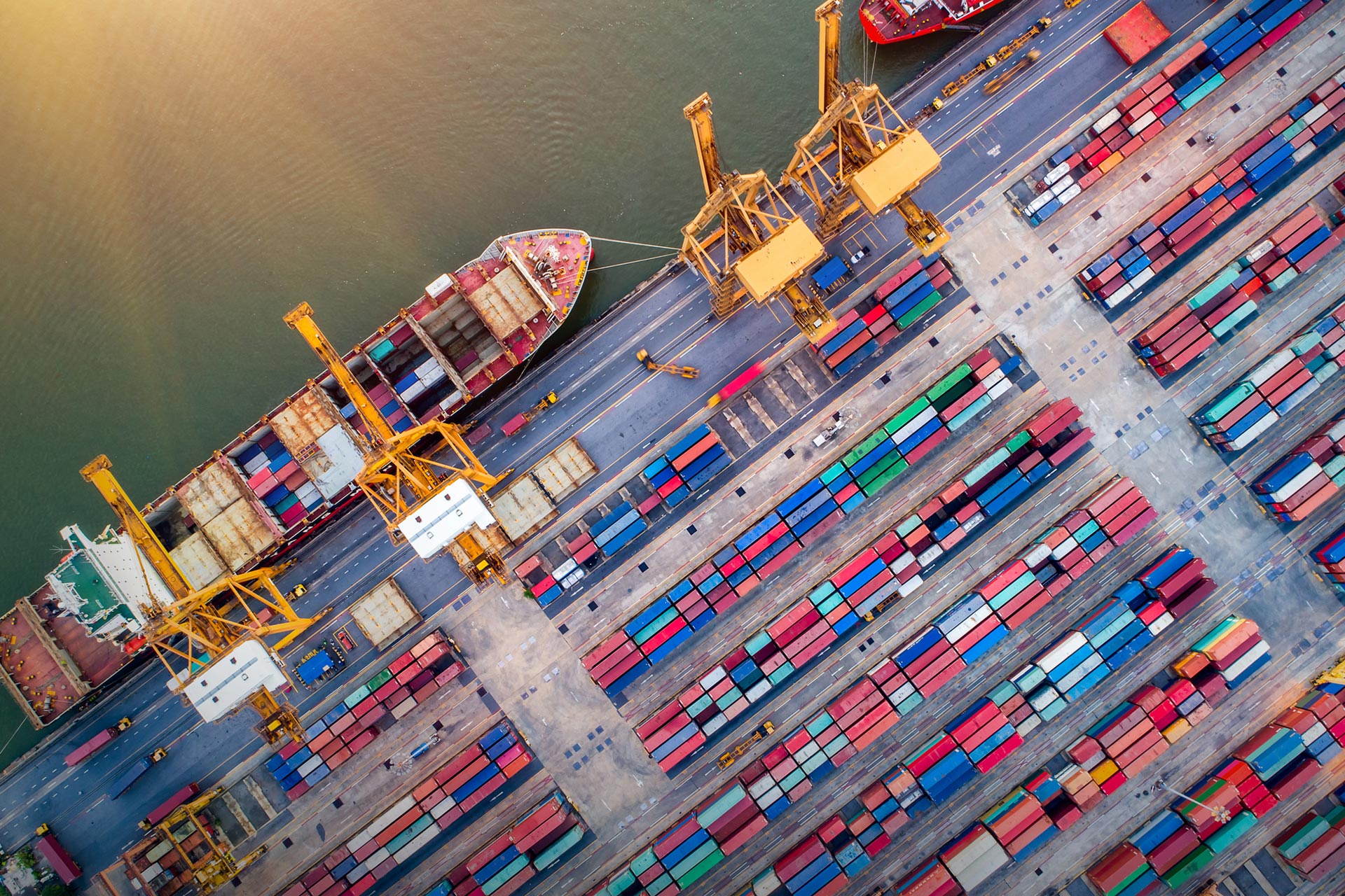 Birds eye view of a port with lots of colourful shipping containers , cranes and large boats.