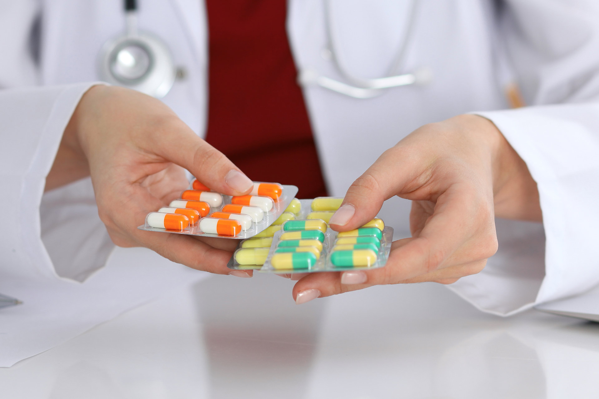 A person in a lab coat is holding two different blister packs of medcation