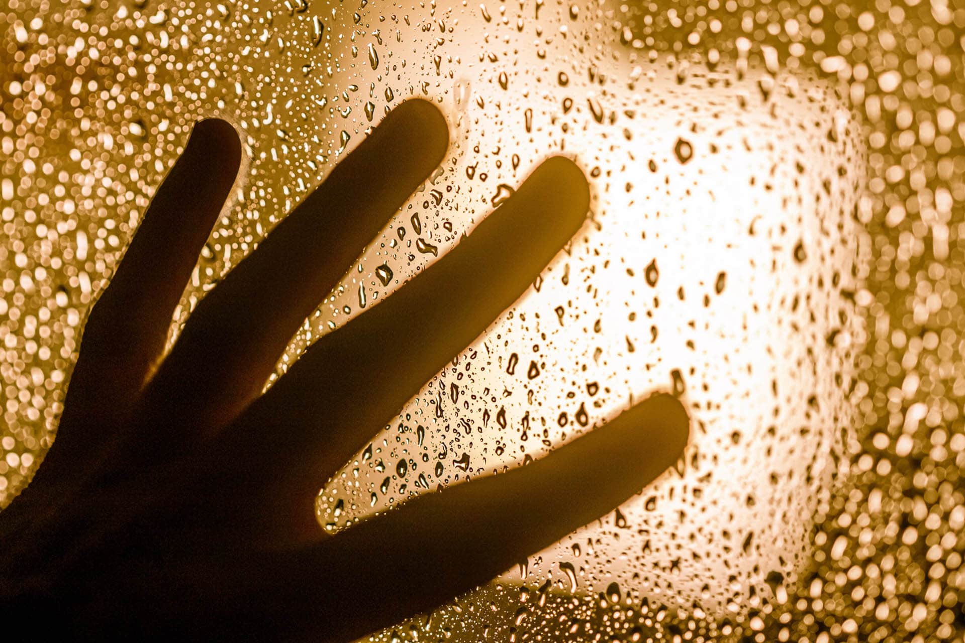 Silhouette of a hand on a window with rain drops