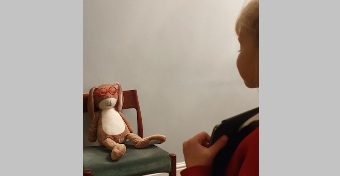 Little girl facing teddy on a chair