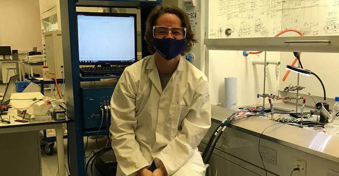 Man sitting in a laboratory setting with a facemask