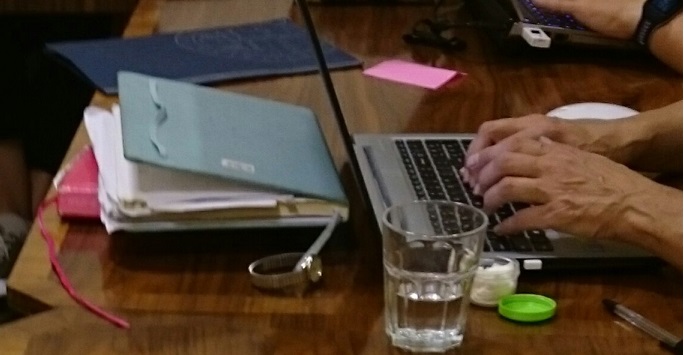 Person typing on a laptop with a glass of water beside them and a watch.