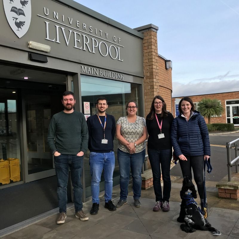 Five people with a dog standing together in front of University entrance