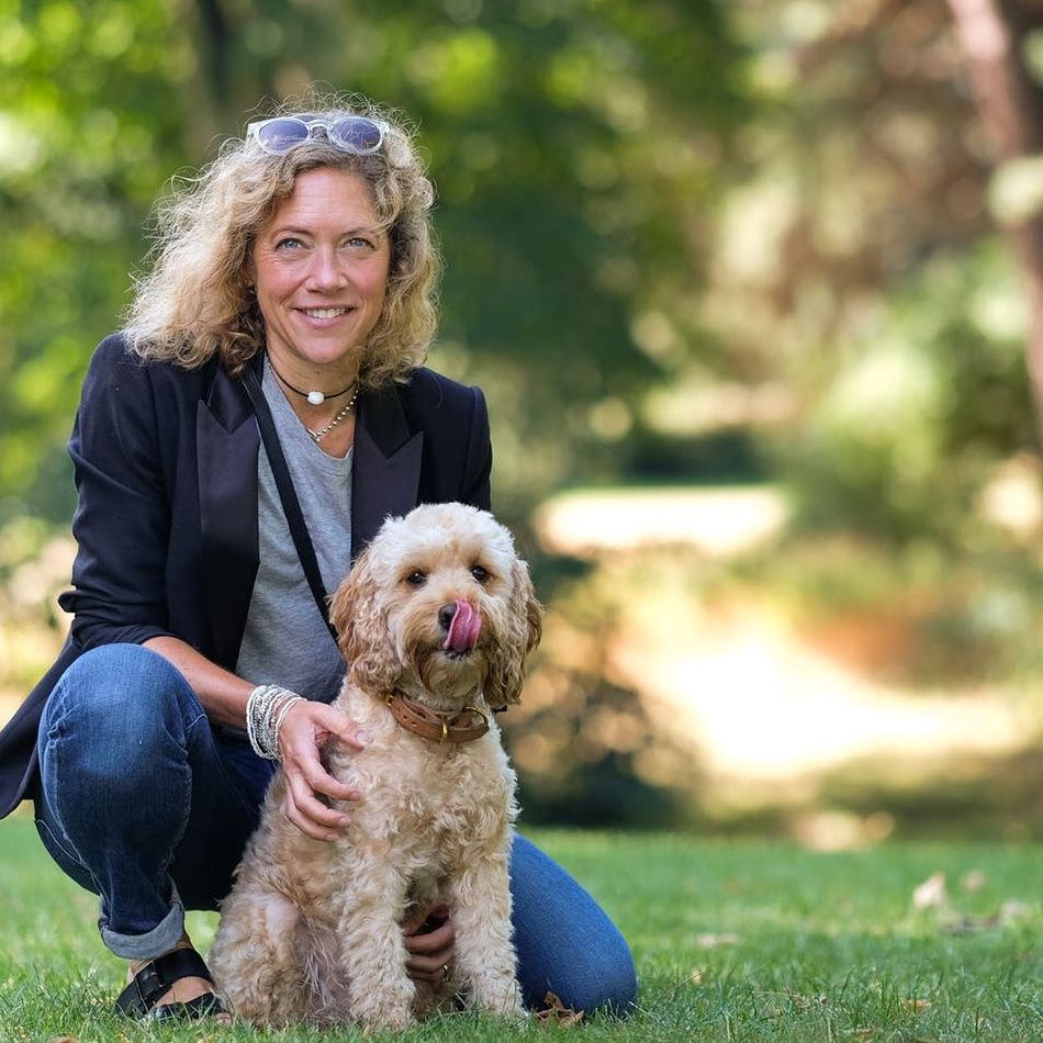 White femaile with blonde hair with a light brown cockerpoo dog in a park