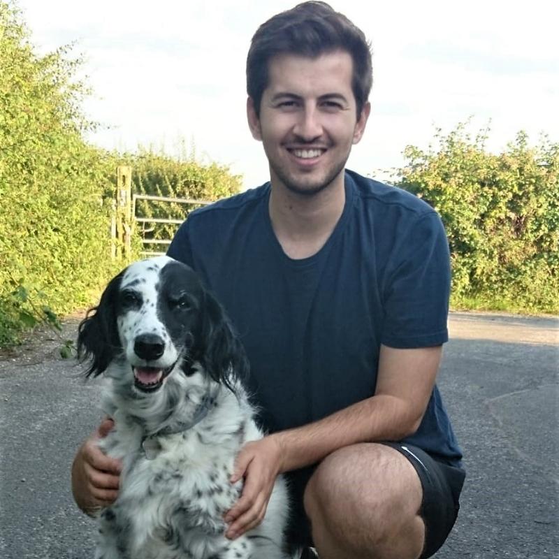 Male with dark brown hair kneeling with black and white dog