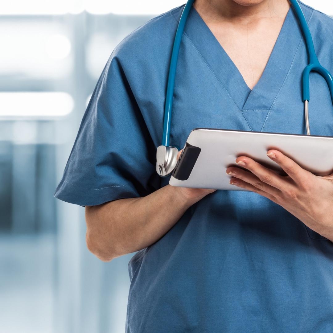 Person wearing blue scrubs in clinical environment looking at a tablet