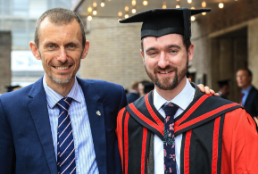 Male in red graduation gown standing with male wearing a suit