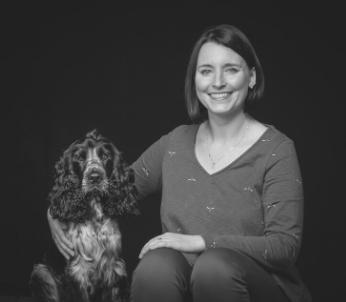 Greyscale image of white female with short dark hair sat with blue roan Cocker Spaniel