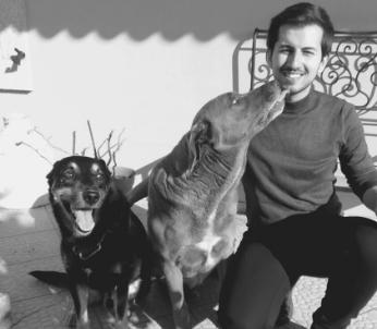 Greyscale image of male with dark hair sat with two dogs