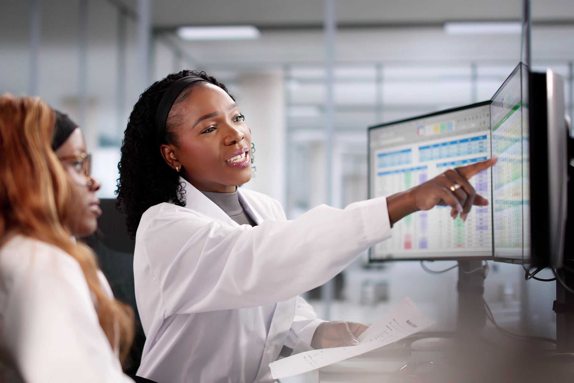Two colleagues study data on a pair of computer screens.