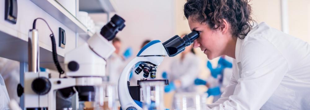 Female in lab coat looking down microscope on laboratory bench