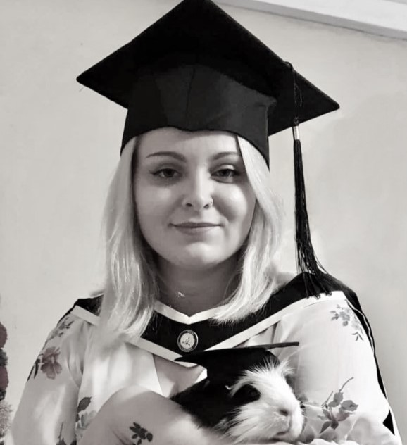 Mary Coles, a PhD student, in her graduation gown, proudly holding her Guinea Pig, also dressed the same.