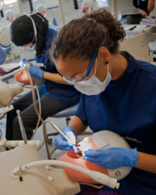 Female undergraduate student performing dental procedure on phantom head in schools teaching lab