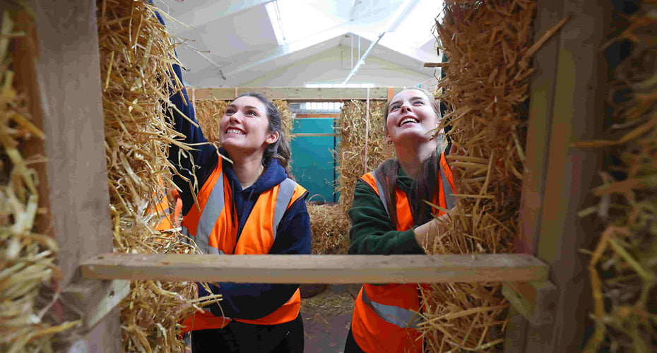 Two female civil engineering students building walls out of straw on the natural building workshop