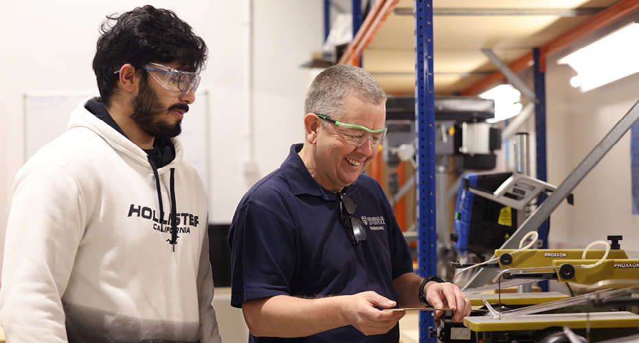 Product design engineering student in workshop being helped by a technician