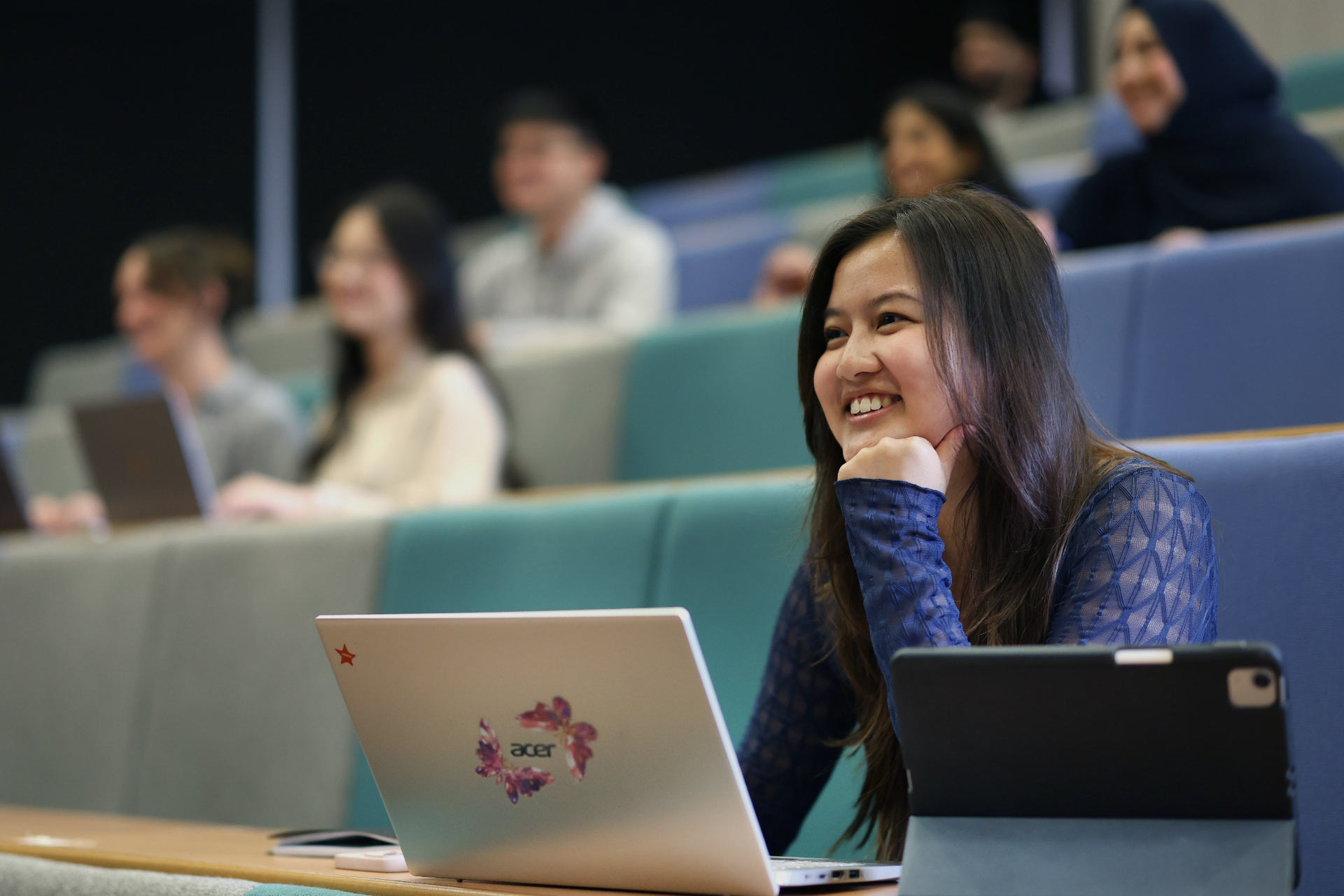 Photo of asian female student sitting in a classroom with her laptop and gadget
