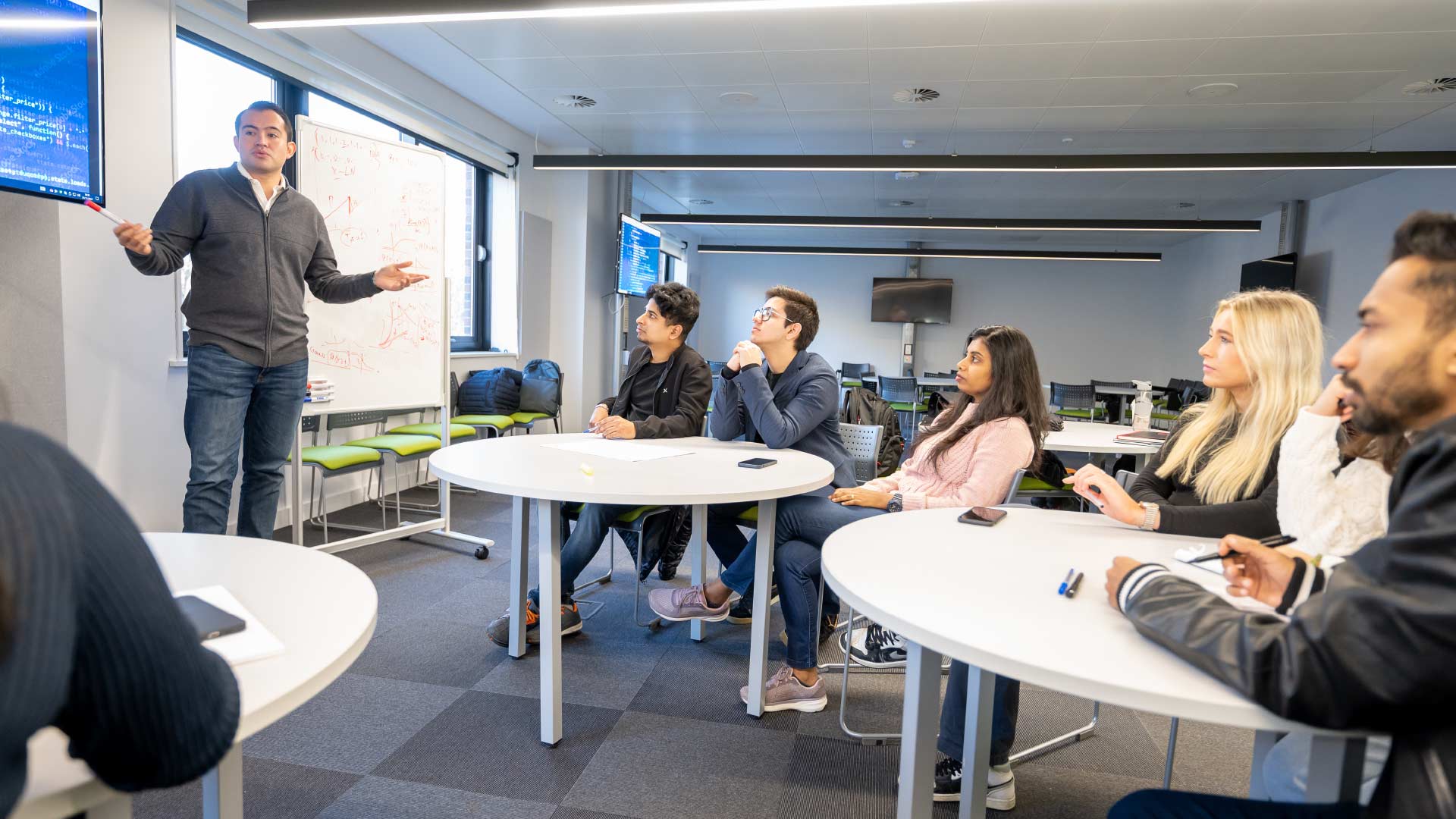 Students in a seminar listening to a lecturer standing at the front of the classroom