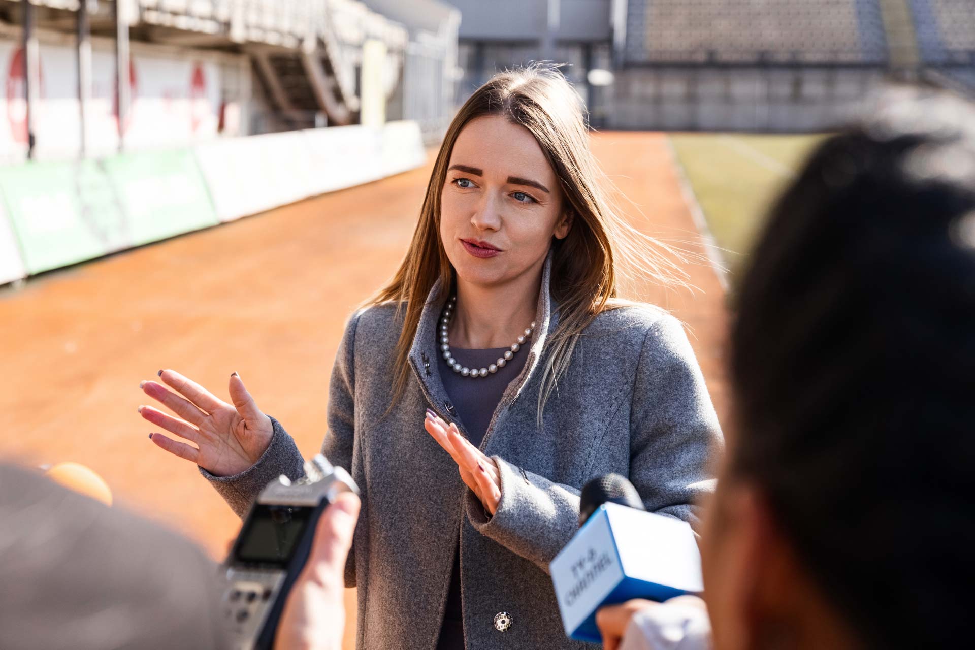 Female football executive speaking to journalists at football ground.
