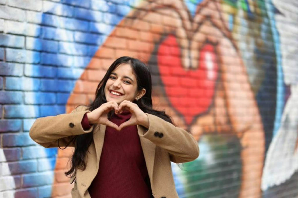 Young woman smiling at the camera with her hands forming a heart shape