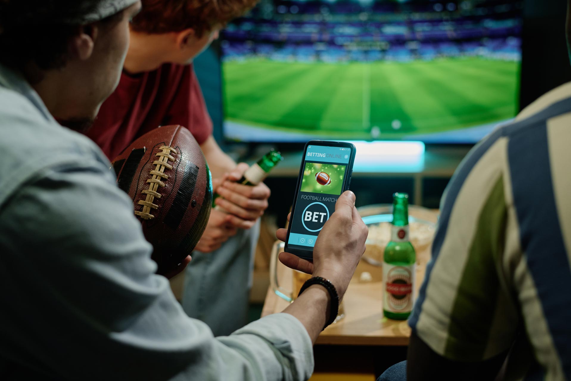 Group of men watch a sports match and one of them bet on his phone