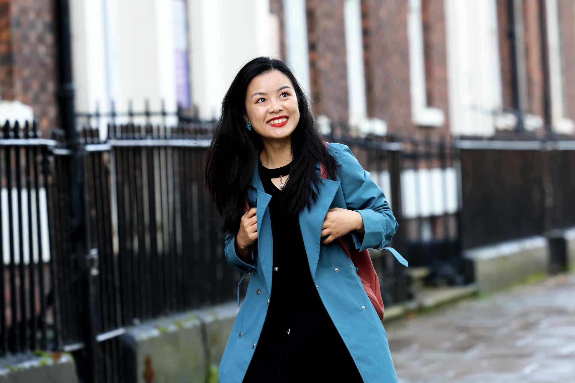 Female student (Xueping Yang) walking walks through campus smiling and carrying a backpack.