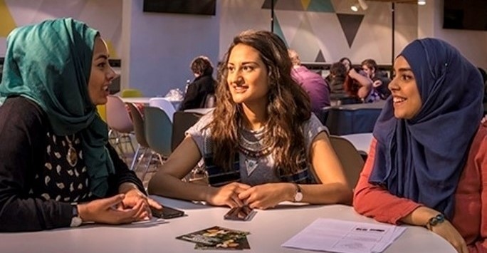 Three students smiling and chatting at a table in the Liverpool Guild of Students