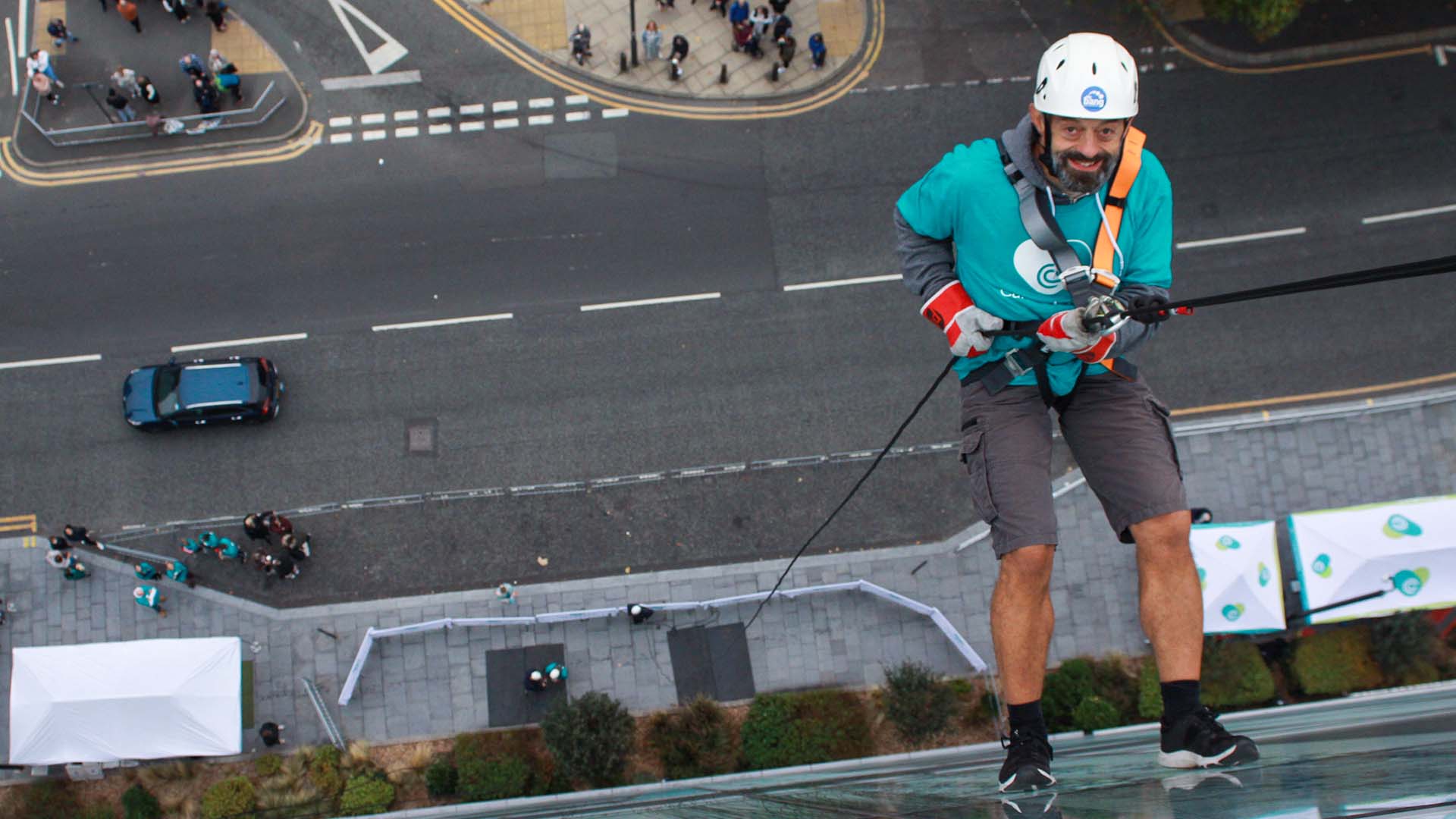 Justin Shanahan abseils down the side of a glass building. Below him is the street.