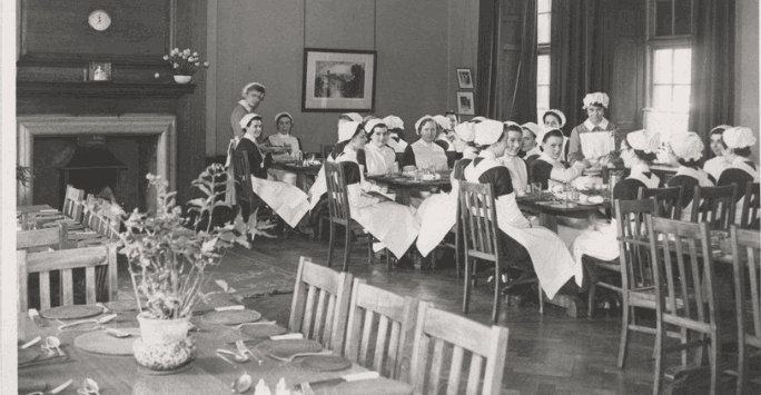 black and white photo of nurses at dining tables with grand fireplace
