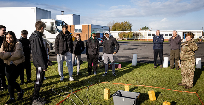 Students stood around a marked square on a field, listening to the direction of an Army Instructor