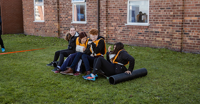 A group of 4 students laughing as one takes a tumble from an improvised platform