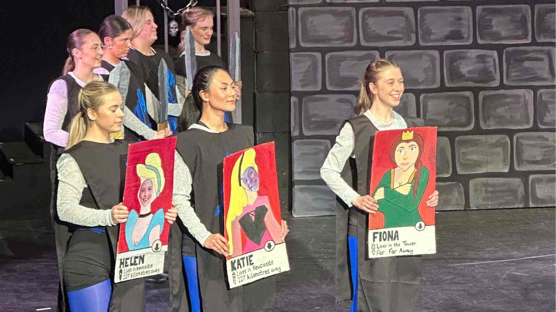 Ensemble cast dressed as knights holding cartoon dating profiles of princesses, including Fiona.