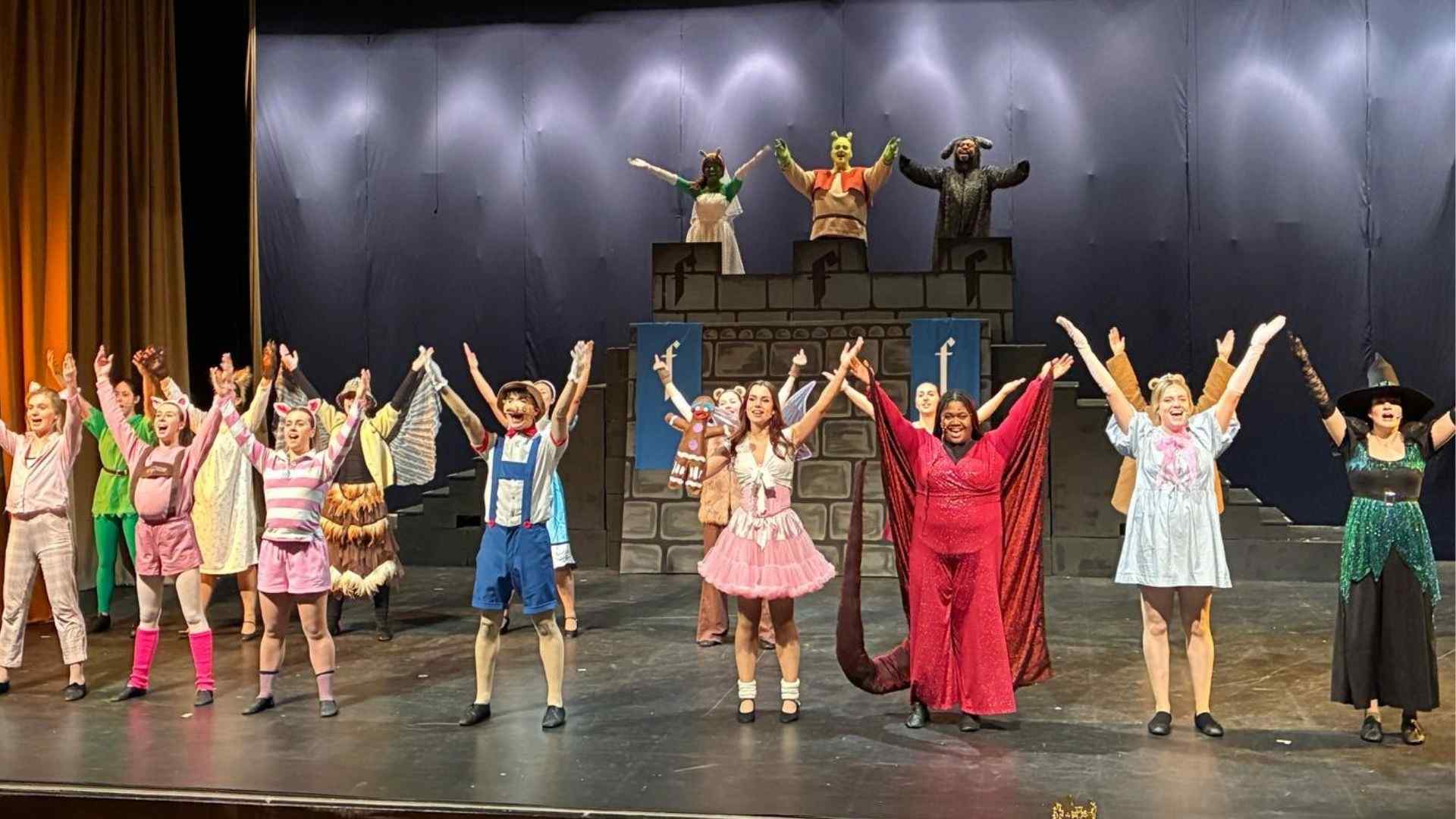 Full cast on stage taking a bow in costume during the final scene of Shrek the Musical.