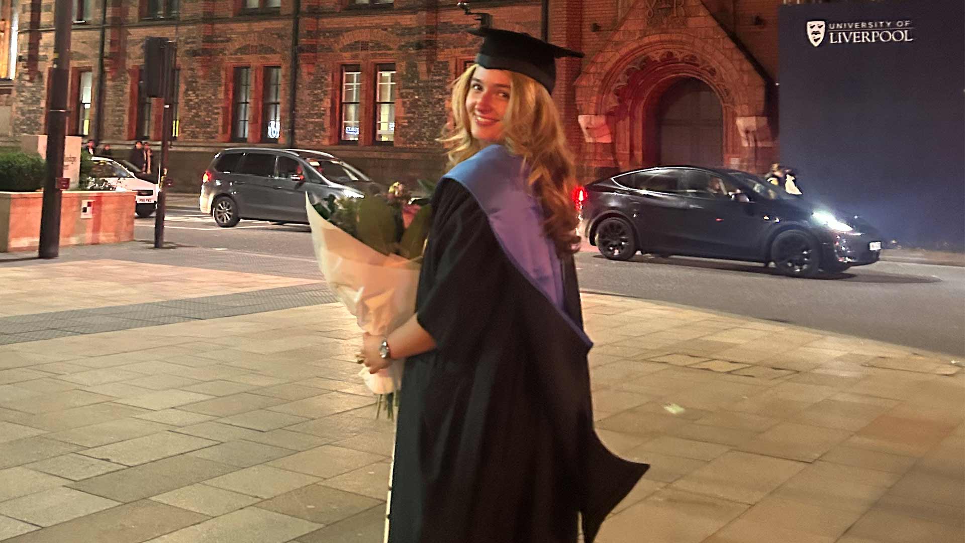 graduate on University Square with bouquet of flowers