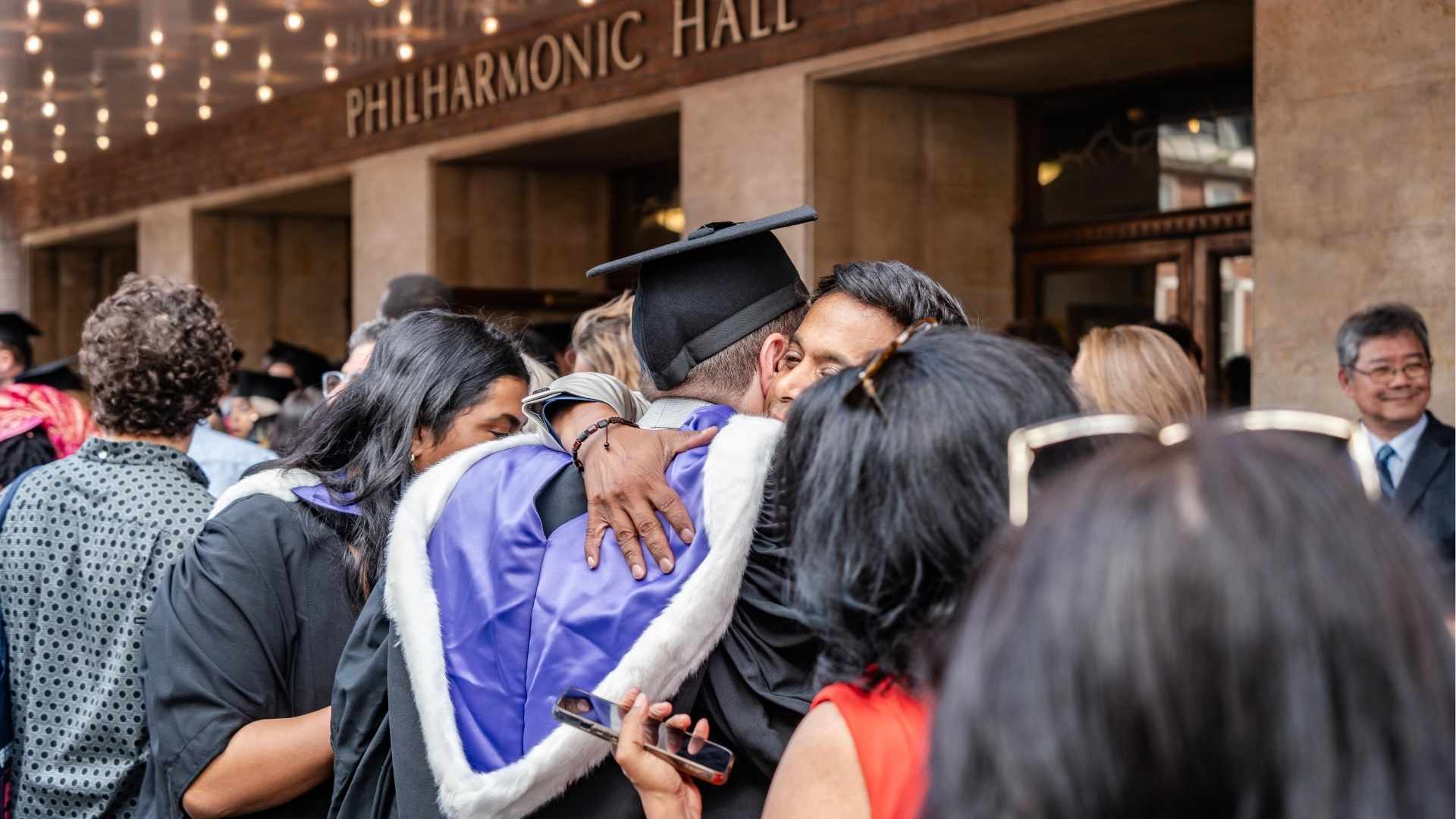 A graduate embraces a loved one outside the Philharmonic Hall