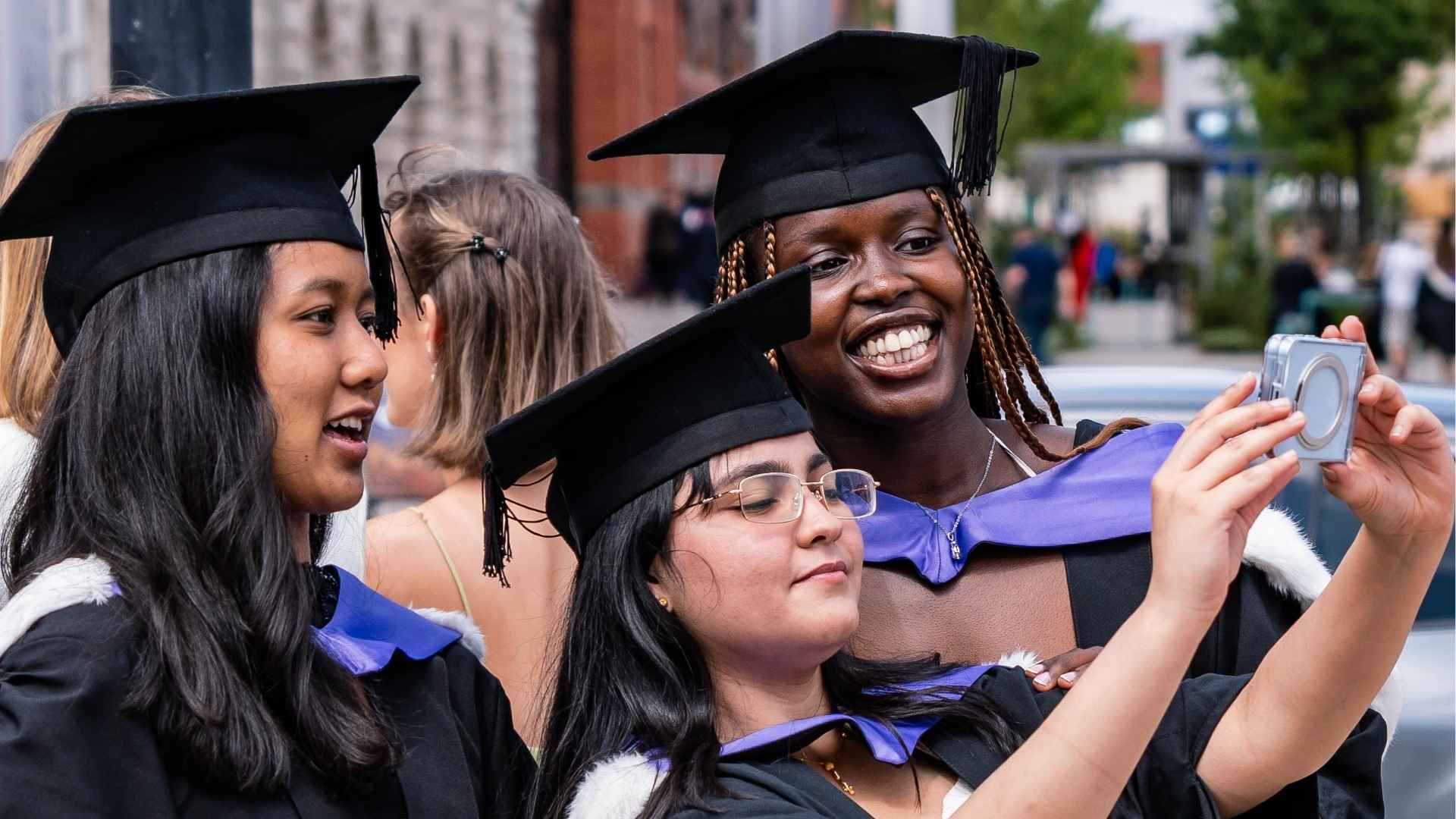 Three graduates in caps and gowns take a selfie