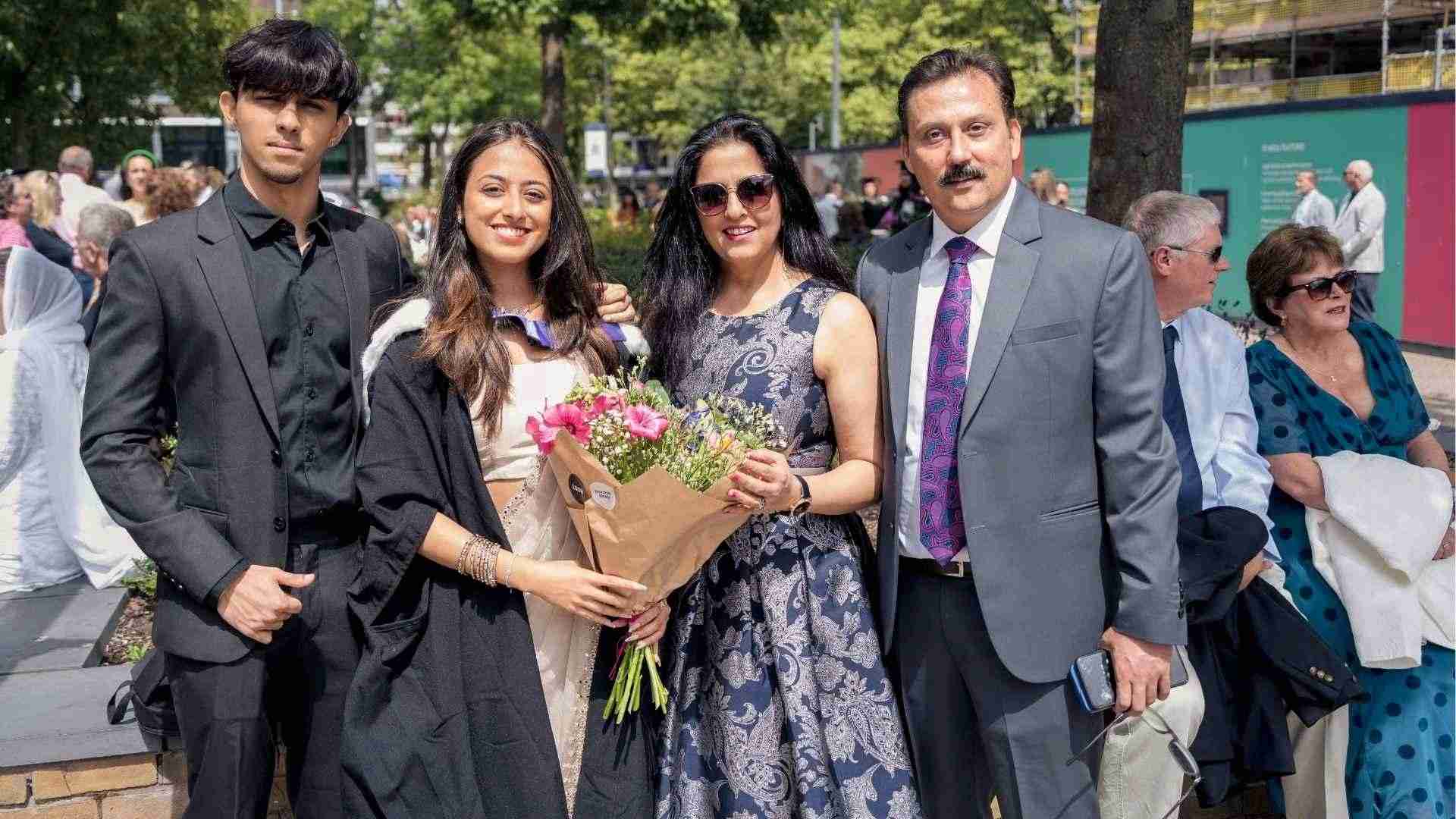 A graduate poses outdoors with her family, holding a bouque