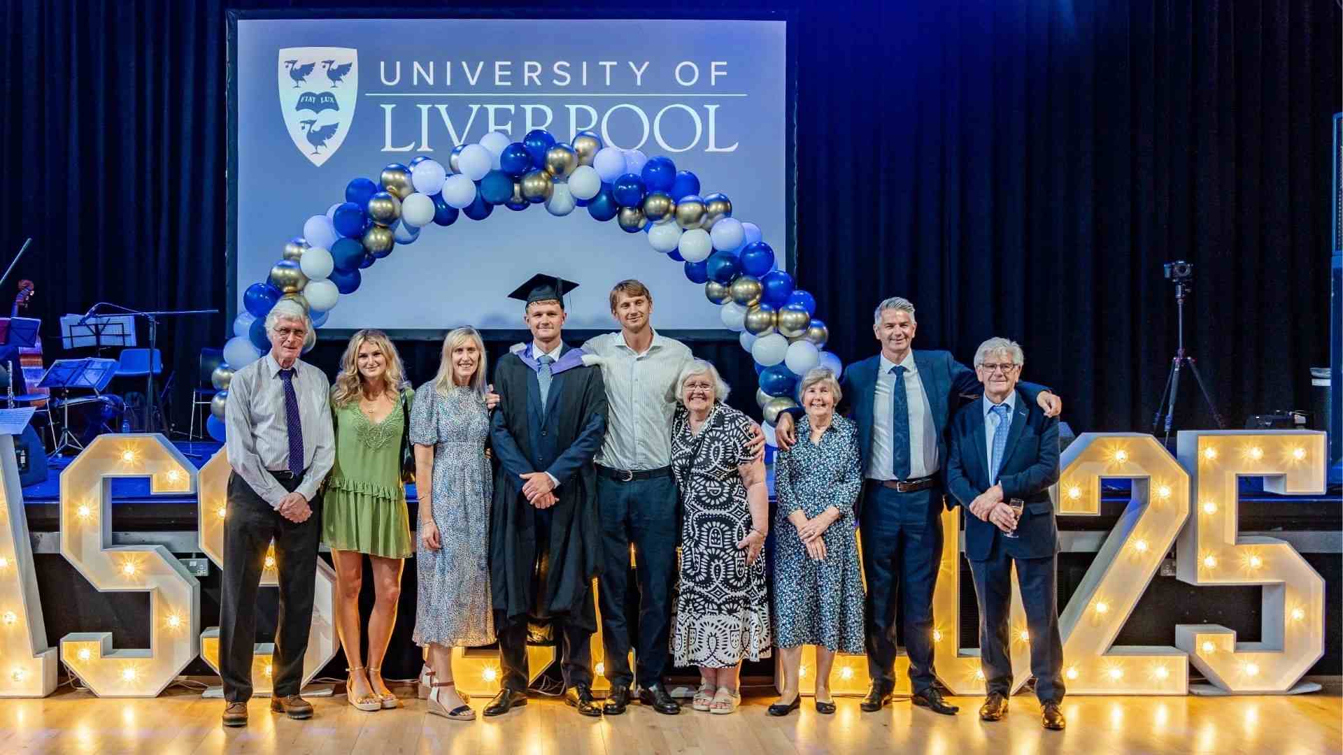 A graduate in gown and hood poses on stage with his family