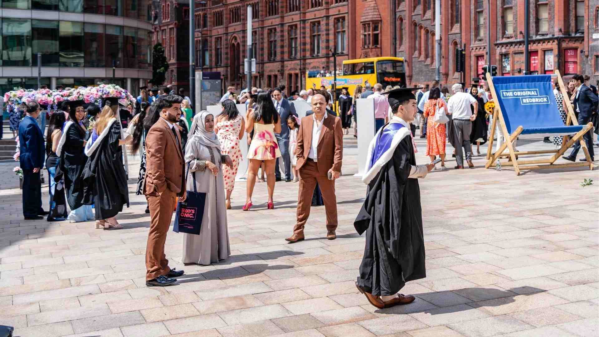 Graduates and families enjoying the sunshine outside the University of Liverpool’s red brick buildings, with a large blue deckchair.