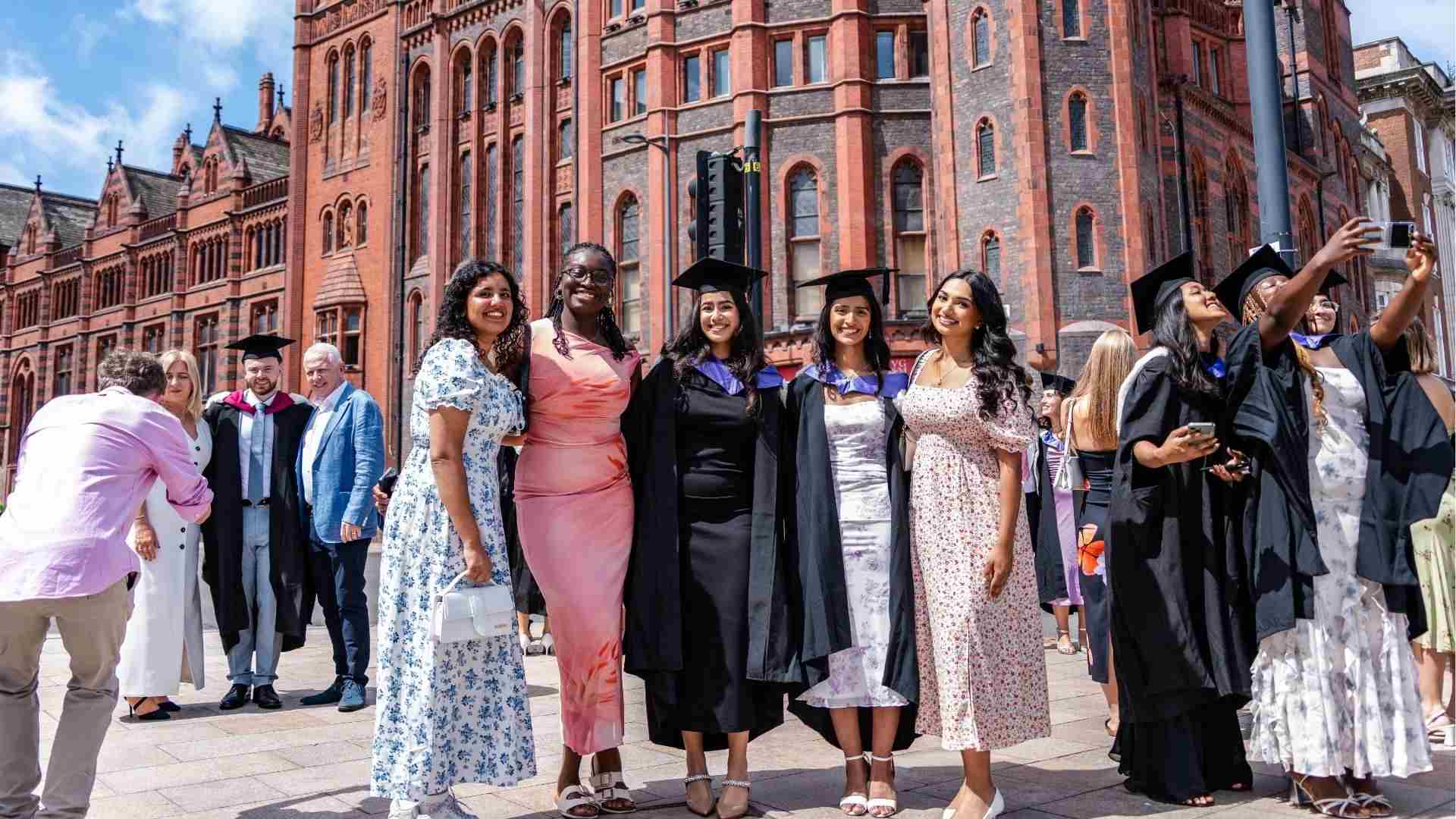 A group of smiling graduates and friends posing for photos in front of the University’s Victoria Building.