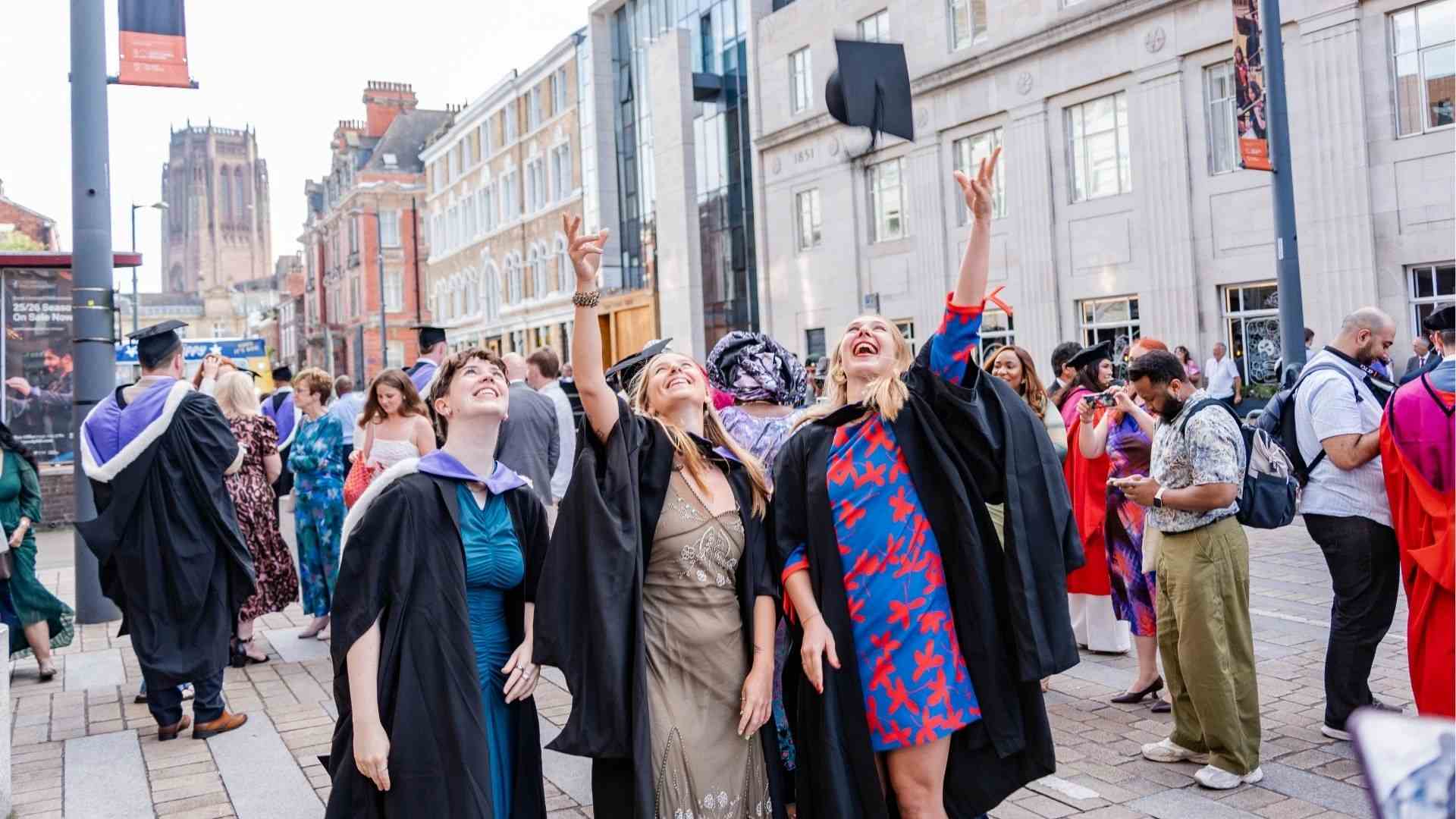 Three graduates laugh and look upward as they throw their caps into the air