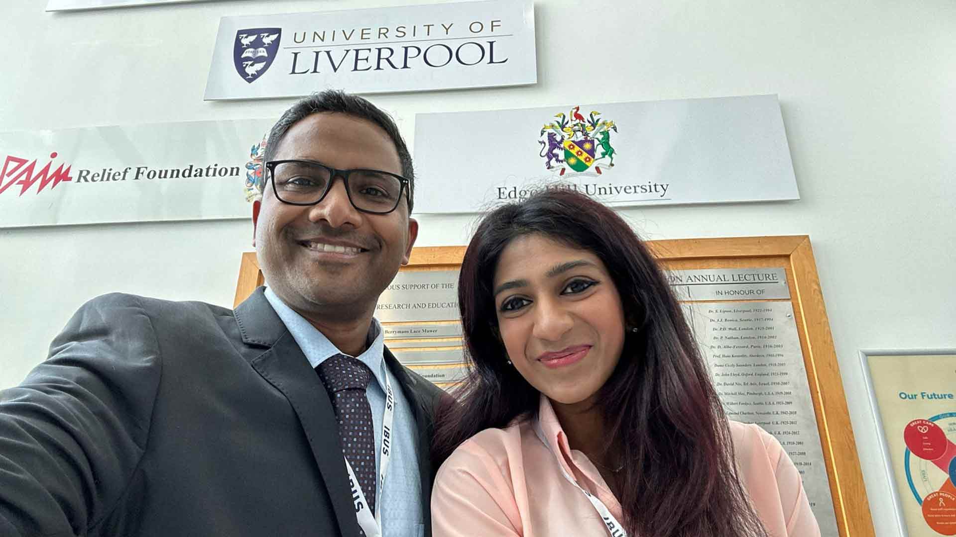 two medical professionals in formalwear with University of Liverpool sign in background