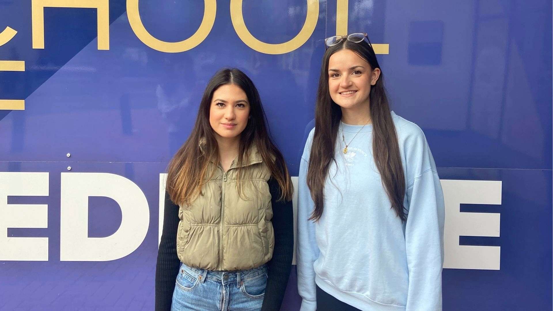 Carmen and Chloe smiling in front of a blue School of Medicine wall