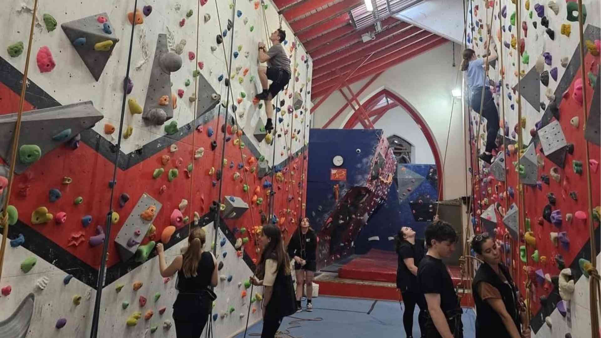 Students climbing indoor rock walls while others watch at Awesome Walls.